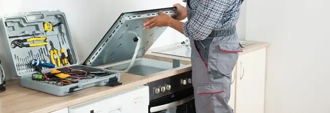 Cooktop repair technician lifting a built-in stovetop for service in Pueblo, CO