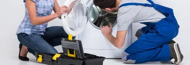 Washer repair technician inspecting a front-load washing machine with tools in Pueblo, CO