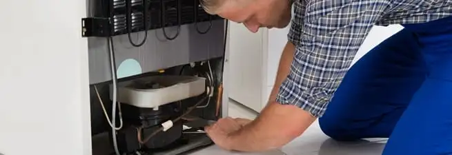 Refrigerator repair technician servicing the compressor and condenser area in Pueblo, CO