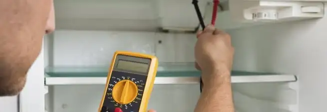 Refrigerator repair technician testing electrical components with a multimeter in Pueblo, CO