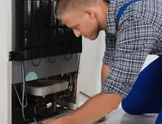 Refrigerator repair technician servicing the compressor and condenser area in Pueblo, CO